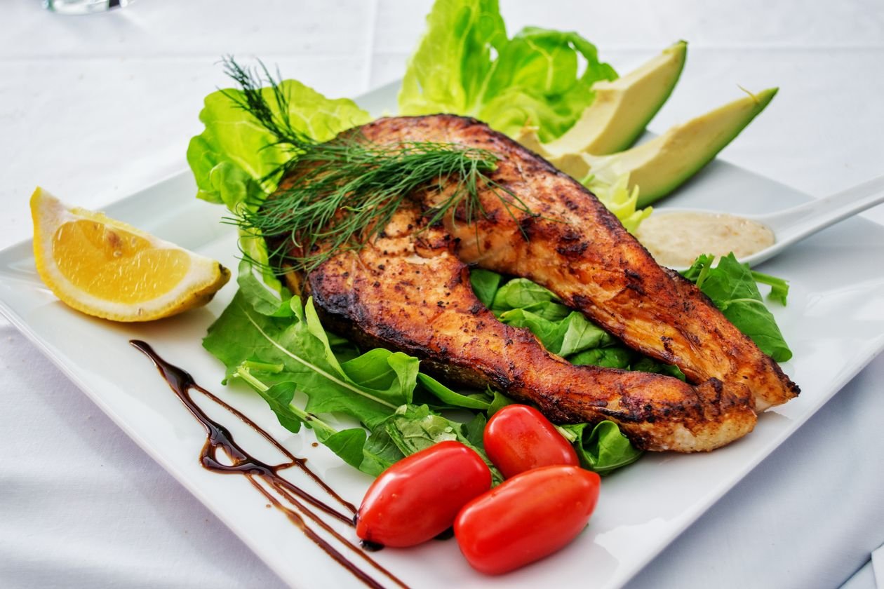 Flaky air fryer salmon fillets with herbs and lemon on a dinner plate.