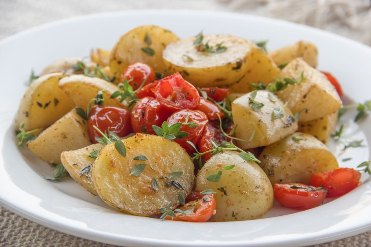 Golden roasted potatoes and sliced sausage with peppers in a baking pan.