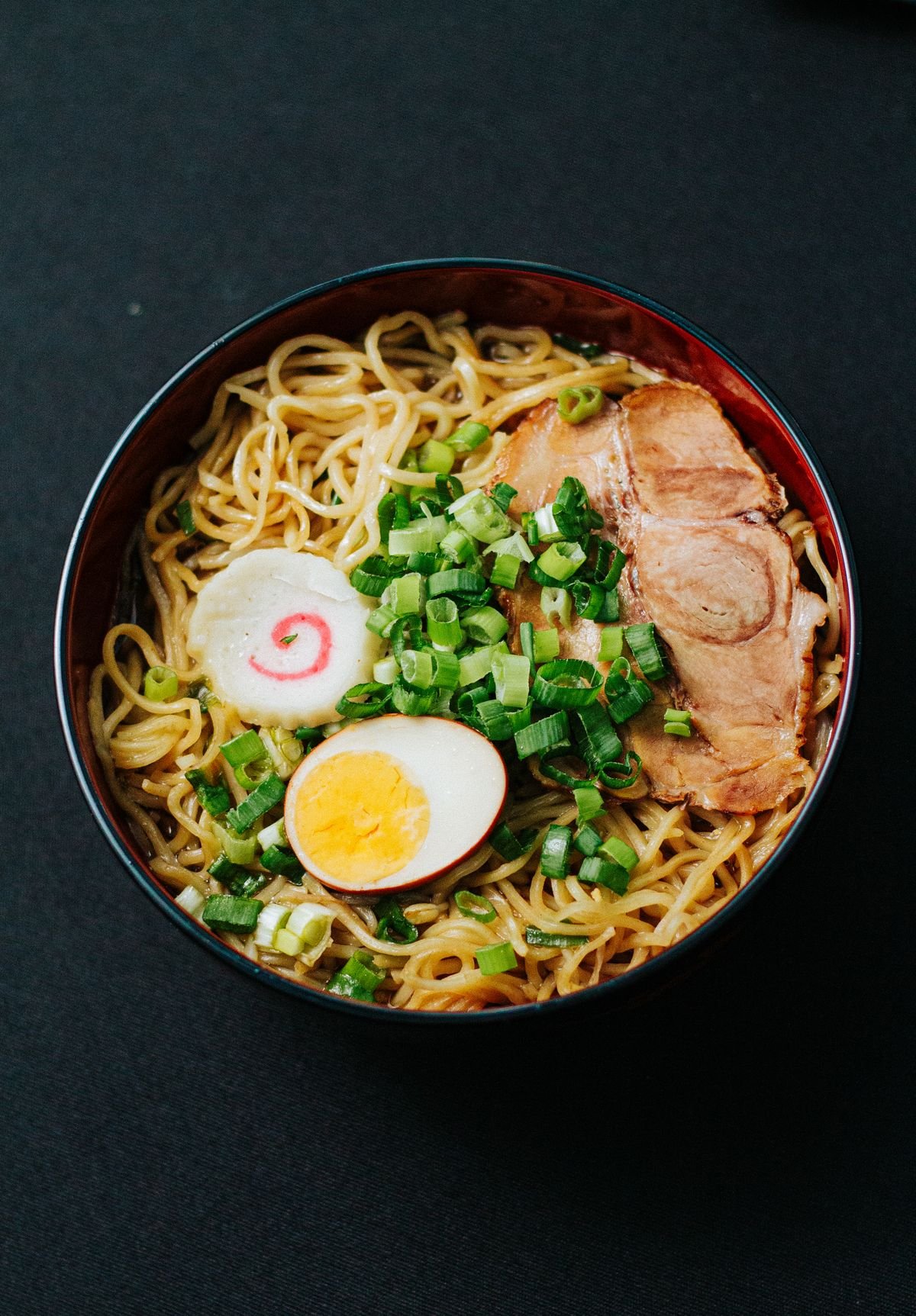 A bowl of ramen noodle stir fry with colorful vegetables and sesame seeds.