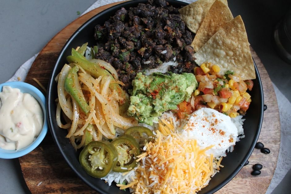 A colorful chicken burrito bowl with rice, black beans, corn, and fresh toppings.
