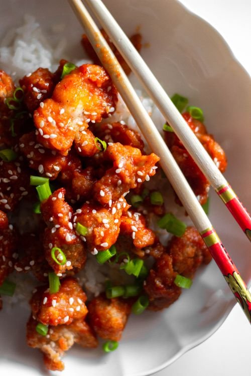 Glossy sesame chicken pieces garnished with sesame seeds and green onions.