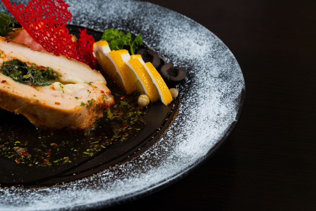A plate of lemon herb chicken breast with rice, lemon slices, and fresh herbs.