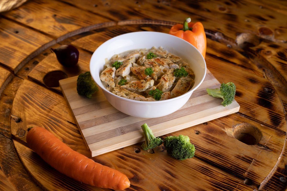 A bowl of chicken tortilla soup topped with tortilla strips, avocado, and cilantro on a wooden board.
