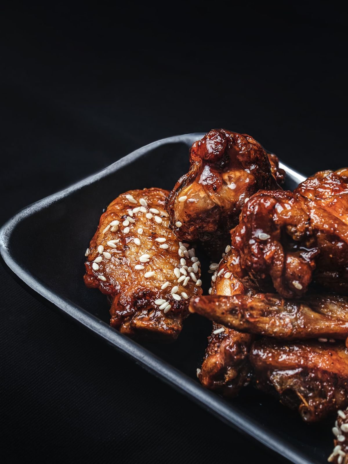 Glazed honey garlic chicken pieces with sesame seeds on a dark plate.