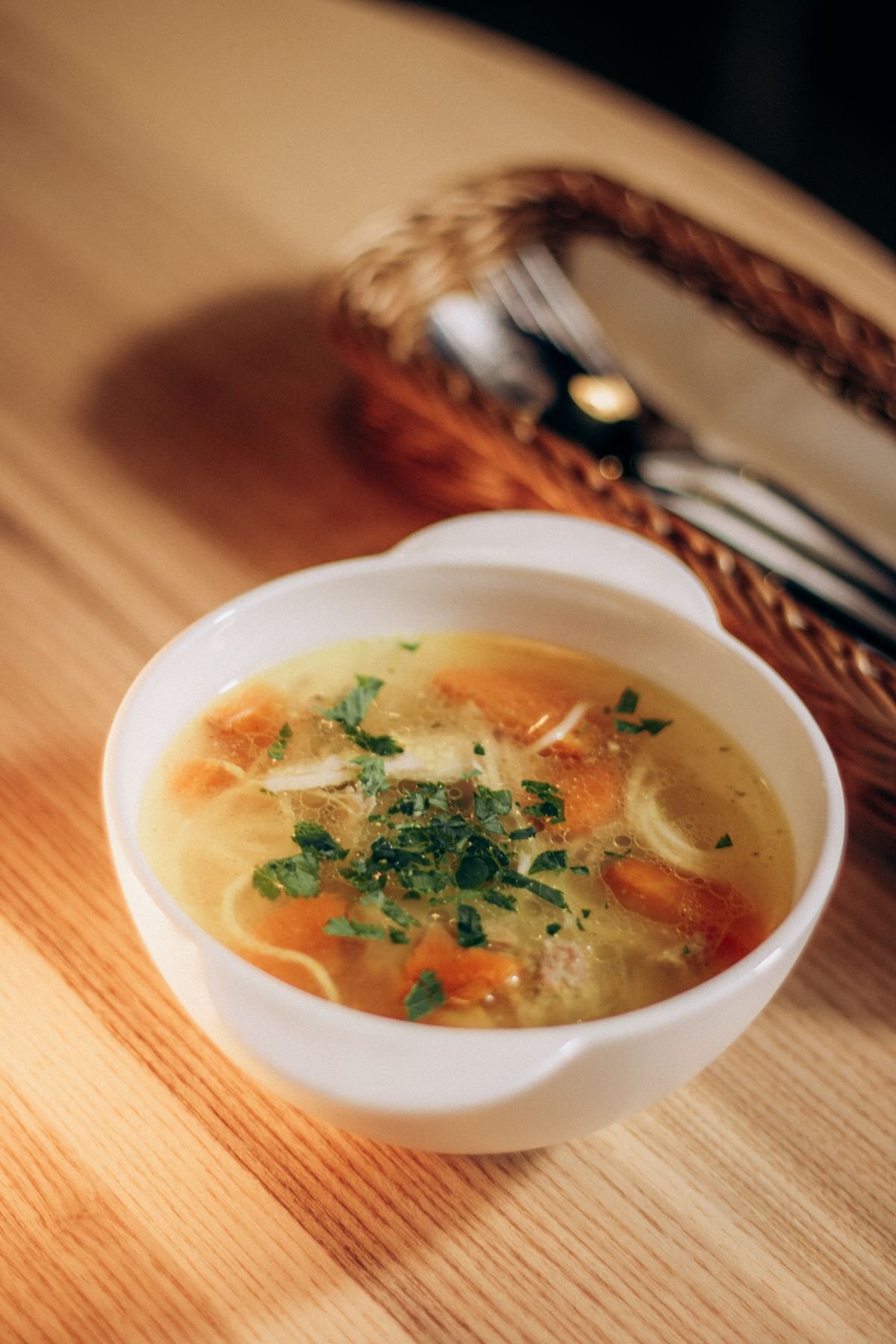 A white bowl of creamy white chicken chili with herbs, served on a wooden table.